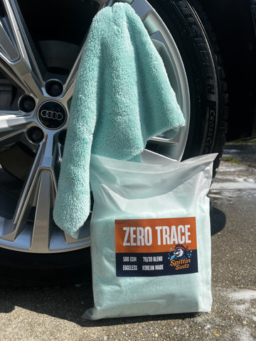 Spittin Sudz Zero Trace premium Korean microfiber finishing towel displayed beside a clean car wheel